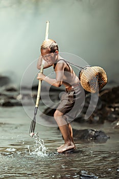 A boy is catching fish in a stream near his home. In the rural areas of Thailand