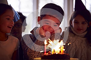 Boy Celebrating Birthday With Group Of Friends At Home Being Given Cake Decorated With Sparkler