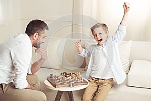 Boy celebrating success in chess game with father near by