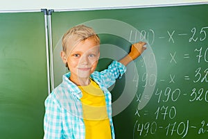 Boy with chalk stands near blackboard and looking