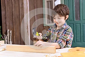 Boy in checkered shirt hammering nail in wooden plank