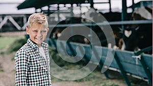 boy in checkered shirt smiling at camera while standing at ranch with cows