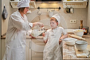 A boy in chef clothes drinks milk from a glass while cooking an apple pie in the kitchen