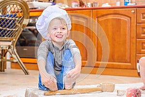 Boy in chefs`s hats near the fireplace sitting on the kitchen floor soiled with flour, playing with food, making mess and having f photo