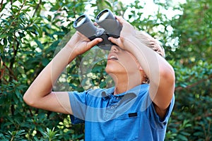 Boy, child with binoculars and surprise, search in nature for learning and fun, forest and adventure at summer camp