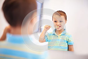 Boy child, brushing teeth and mirror in bathroom for cleaning, hygiene or health for routine in home. Kid, toothbrush or