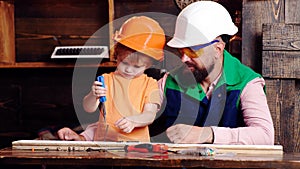 Boy, child busy in protective helmet learning to twist the screws with a screwdriver with dad. Workshop and handyman