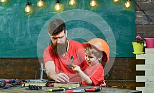 Boy, child busy in protective helmet learning to use hammer with dad. Father with beard teaching little son to use tools
