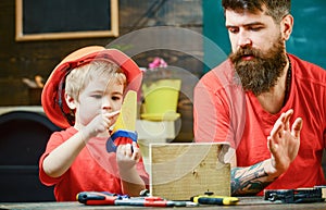 Boy, child busy in protective helmet learning to use handsaw with dad. Educational games concept. Father, parent with