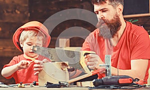 Boy, child busy in protective helmet learning to use handsaw with dad. Masculine duties concept. Father, parent with