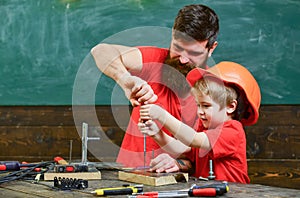 Boy, child busy in protective helmet learning to use screwdriver with dad. Father, parent with beard teaching little son