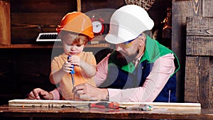 Boy, child busy in protective helmet learning to use screwdriver with dad. Teamwork in workshop concept. Father, parent