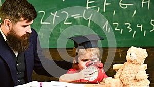 Boy, child on calm face holds alarm clock while teacher talk to kid. Individual lesson concept. Teacher with beard