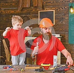 Boy, child cheerful holds bolts or screws, having fun while handcrafting with dad. Father, parent with beard in helmet