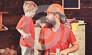 Boy, child cheerful holds spanner wrench, learning use tools with dad. Father, parent with beard in protective helmet