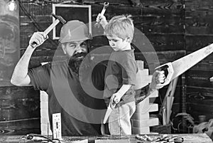 Boy, child cheerful holds toy saw, having fun while handcrafting with dad. Father, parent with beard in protective