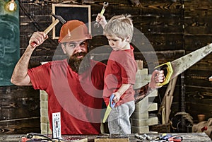 Boy, child cheerful holds toy saw, having fun while handcrafting with dad. Father, parent with beard in protective