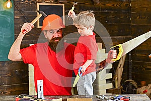 Boy, child cheerful holds toy saw, having fun while handcrafting with dad. Father, parent with beard in protective