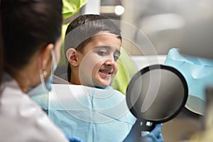 Boy child with a dentist looks his teeth in the mirror