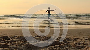 Boy child is jumping on a sea beach at sunset. Hyperactive boy run and jump on beach sand smiling.