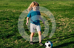 Boy child playing football on football field. Kid playing soccer. Kid kicking a football ball on a grass.