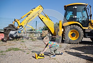 Boy child plays with a toy loader on the background of a real big yellow excavator
