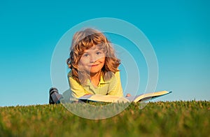 Boy child reading book, lying down on green grass.