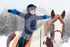 A boy child rides a horse in winter through a snowy forest