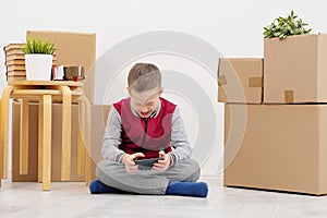 The boy child sits on the floor and plays on the smartphone. Boxes with cargo on a white background.