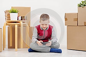 The boy child sits on the floor and plays on the smartphone. Boxes with cargo on a white background.