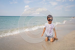 boy child in striped shorts and a white T-shirt walks on sandy beach and in sunglasses