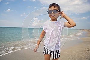 boy child in striped shorts and a white T-shirt walks on sandy beach and in sunglasses