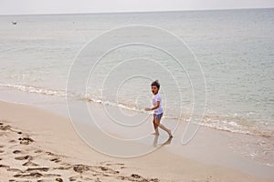 boy child in striped shorts and a white T-shirt walks on sandy beach and in sunglasses