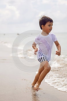 boy child in striped shorts and a white T-shirt walks on sandy beach and in sunglasses