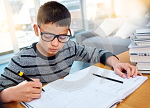 Boy child, student and writing in book for studying, education and learning homework on table at home. Smart little kid