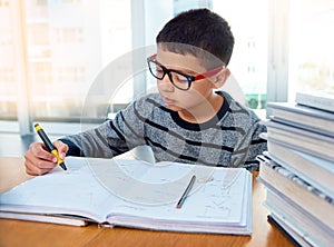Boy child, student and writing for studying, homework or learning in education with book on table at home. Smart little