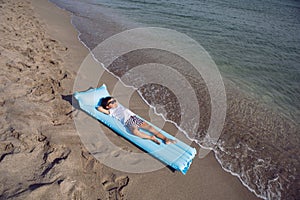 boy child in a white T-shirt and striped swimming trunks and sunglasses is lying on a blue inflatable mattress on the