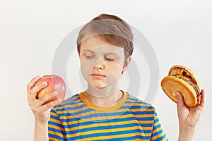 Boy chooses between hamburger and healthy diet on white background