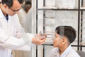 Boy choosing eyeglasses frames and talking with ophthalmologist in optical store, Child doing eye test checking examination with