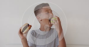 Boy choosing healthy or unhealthy food. Boy making a choice between apple and burger, healthy or fast, junk food, chose