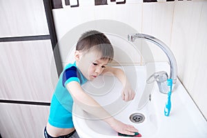 Boy cleaning in bathroom wash sink, child doing up housework helping mother with sanitary cleanness of home