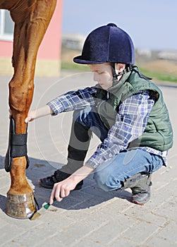 Boy cleans a hoof of horse