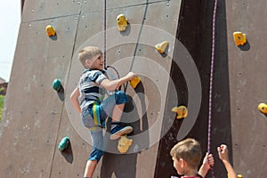 A boy in climbing equipment conquers the top of an artificial tower for climbers in a sports extreme recreation park photo