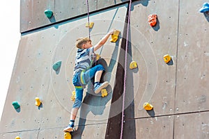 A boy in climbing equipment conquers the top of an artificial tower for climbers in a sports extreme recreation park photo