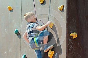 A boy in climbing equipment conquers the top of an artificial to photo