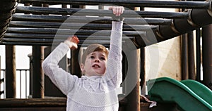 Boy climbing monkey bars on a jungle gym outdoors in a kids activity park during summer. Strong, happy and wild child