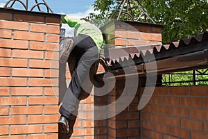 Boy is climbing over brick fence outside from home yard.