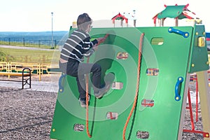 Boy climbs on a climbing wall holding the rope on the Playground.