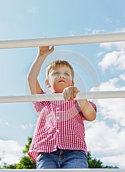 Boy climbs up on a ladder, a bottom view, in the open air against the blue of the sky