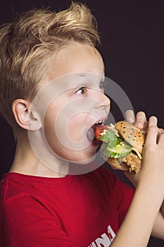 Boy close-up with open mouth eats a delicious burger with chicken